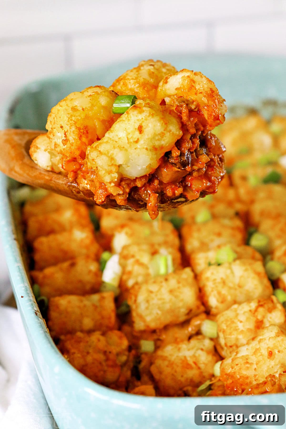 Fiesta Tater Tot Bake 6 A large wooden spoon scooping a portion of Taco Tater Tot Casserole, showcasing the layers of meat, cheese, and crispy tots.