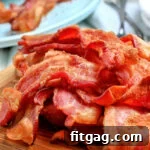 Air fryer bacon piled high on a wooden board with a blue plate in the background.