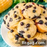 Top-down view of corn muffin recipe with blueberries on white plate with corn and yellow flowers behind the plate