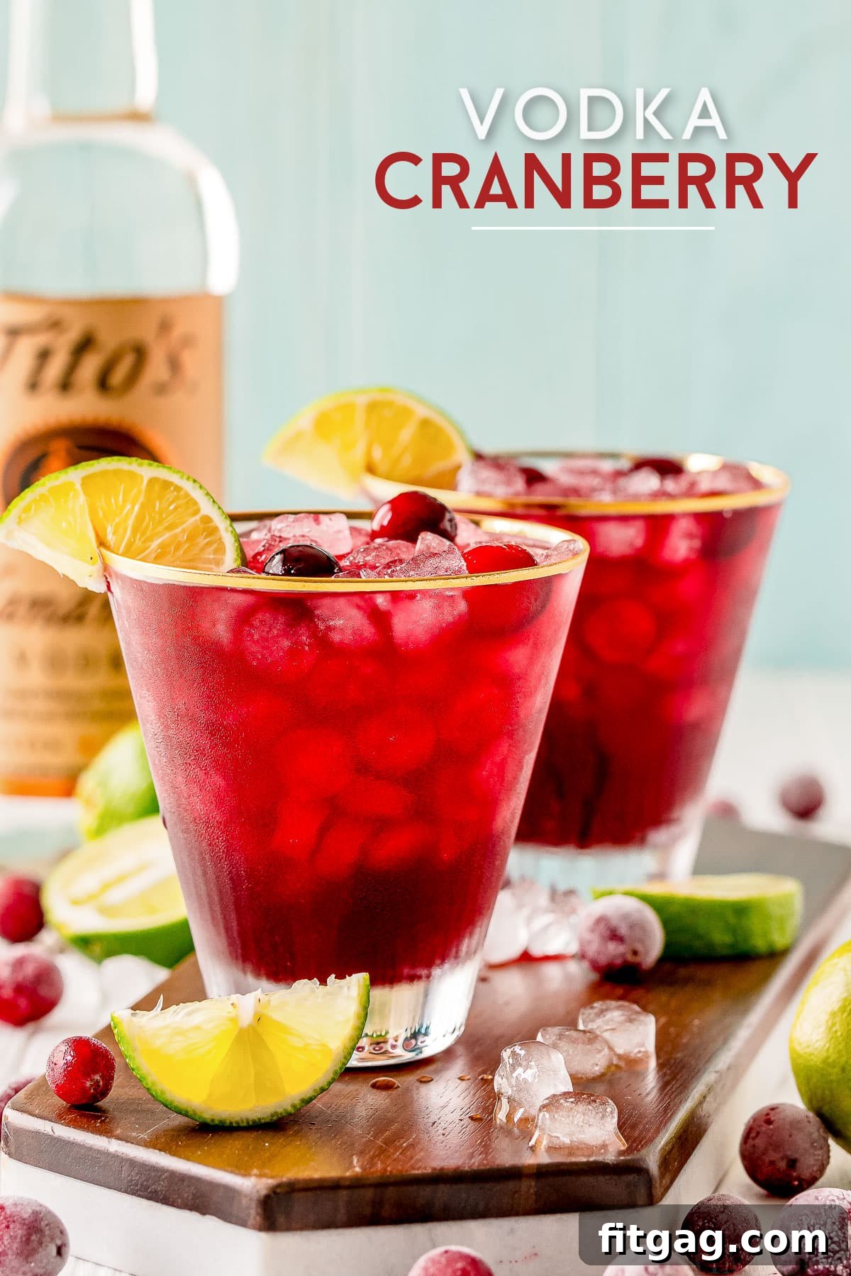Two glasses of Vodka Cranberry with lime wedges and cranberries, vodka bottle in background