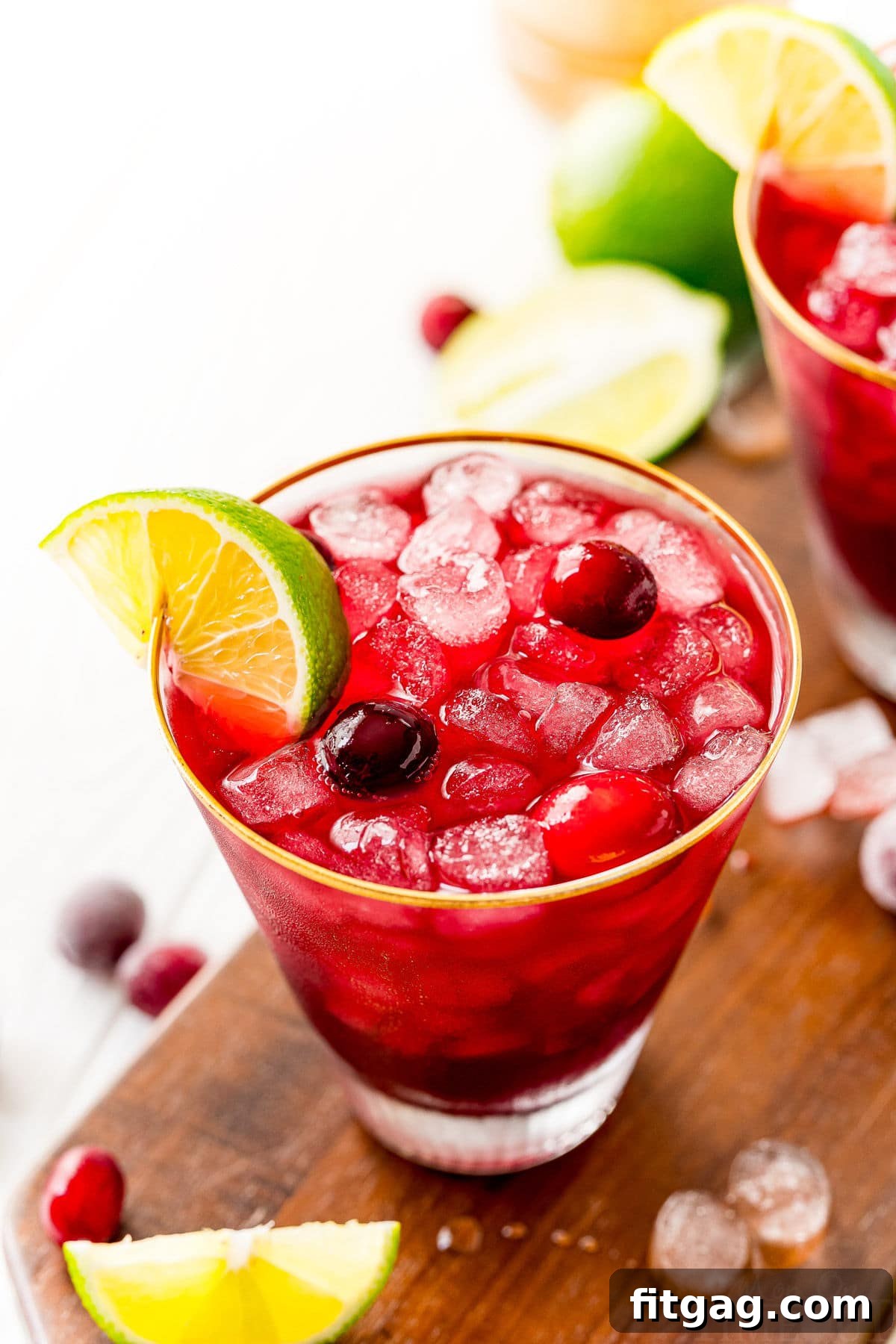 Vodka Cranberry cocktail in glass with lime wedge and cranberries on dark wood board