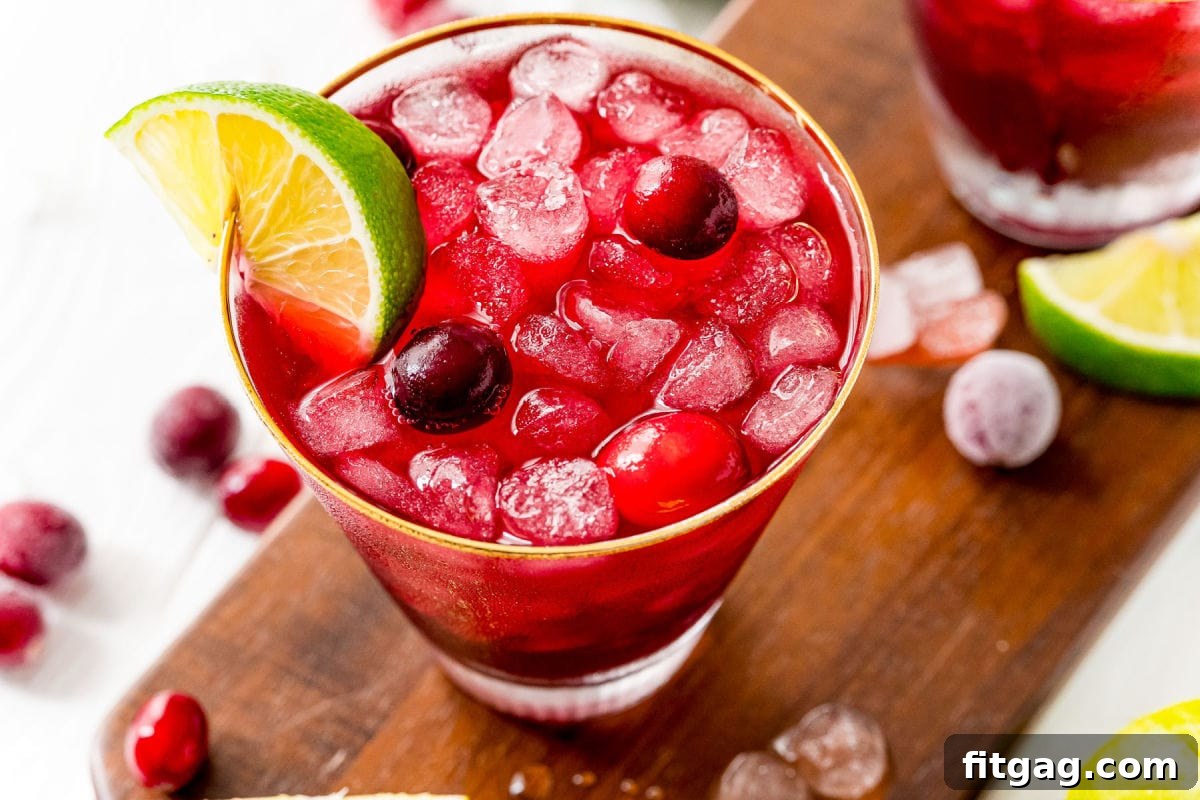 Vodka Cranberry cocktail in glass with lime wedge and cranberries on dark wood board