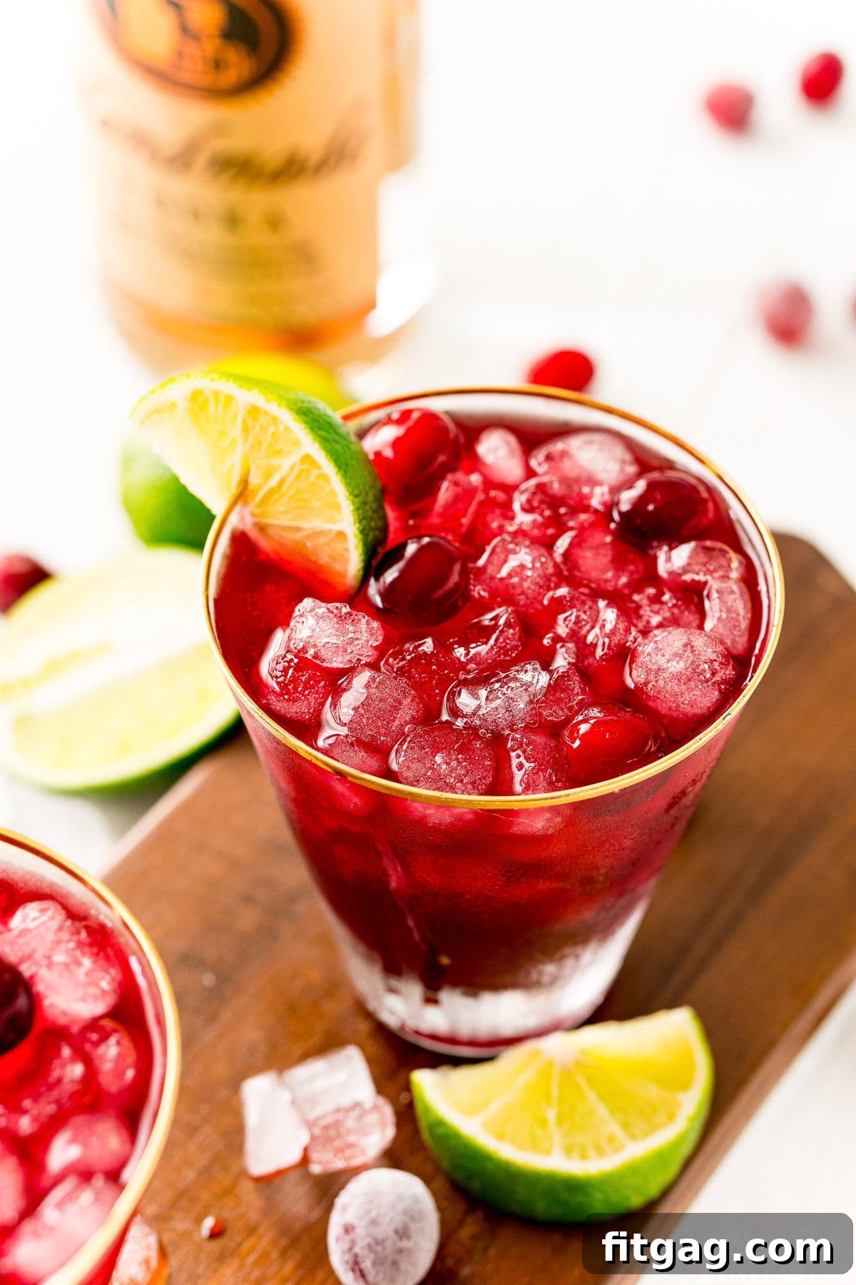 Vodka Cranberry cocktail in glass with lime wedge and cranberries on dark wood board