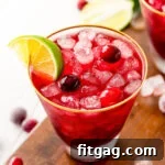 Vodka Cranberry cocktail in glass with lime wedge and cranberries on dark wood board