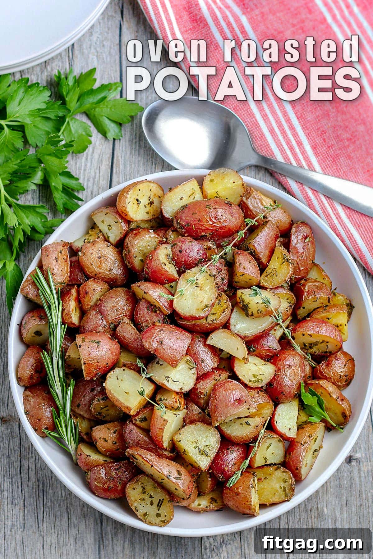 white plate with perfectly crispy roasted potatoes garnished with fresh herbs and a red towel in the upper right corner