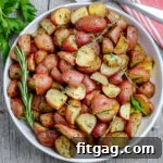 white plate with roasted potatoes garnished with fresh herbs and red towel underneath