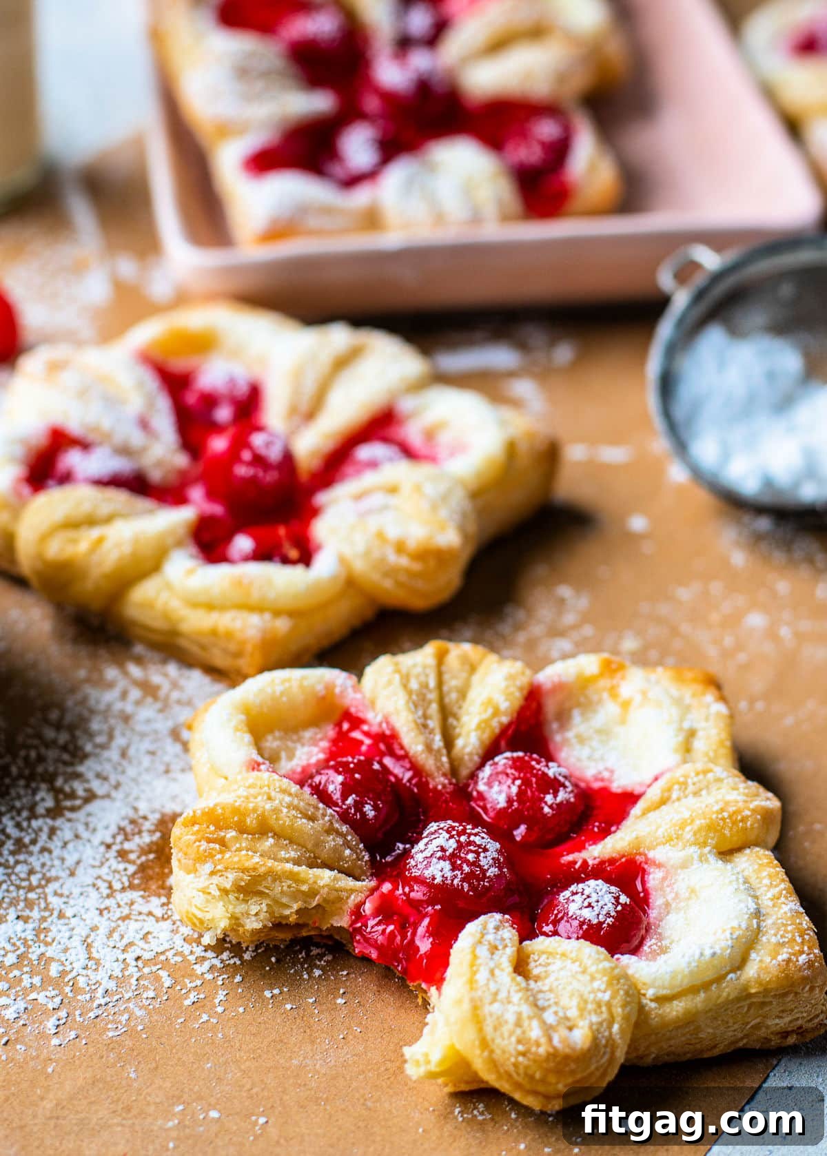 cherry danish with bite taken on brown parchment paper and danishes in the background