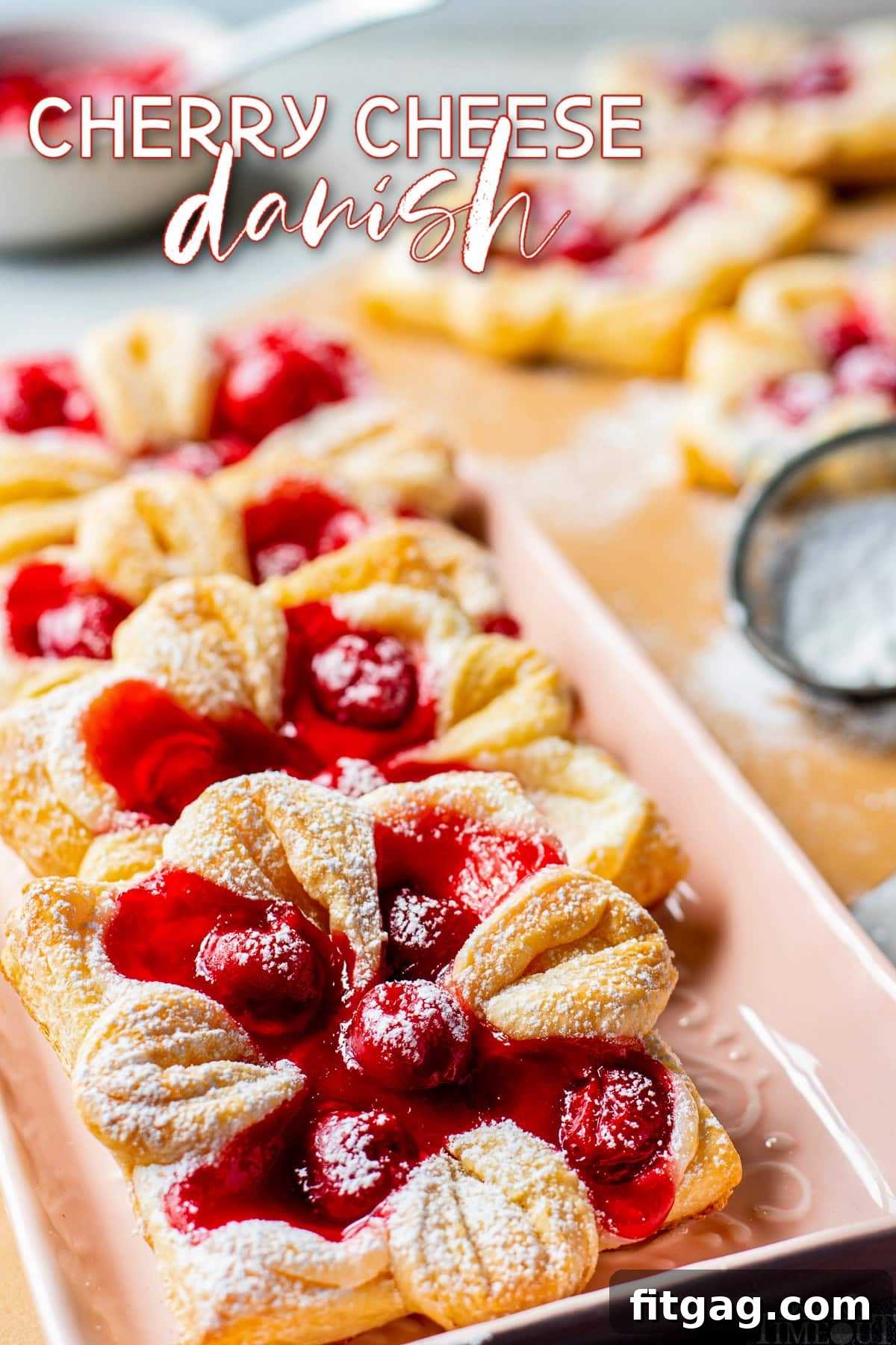 cherry cheese danishes on light pink tray dusted with powdered sugar and text overlay at the top