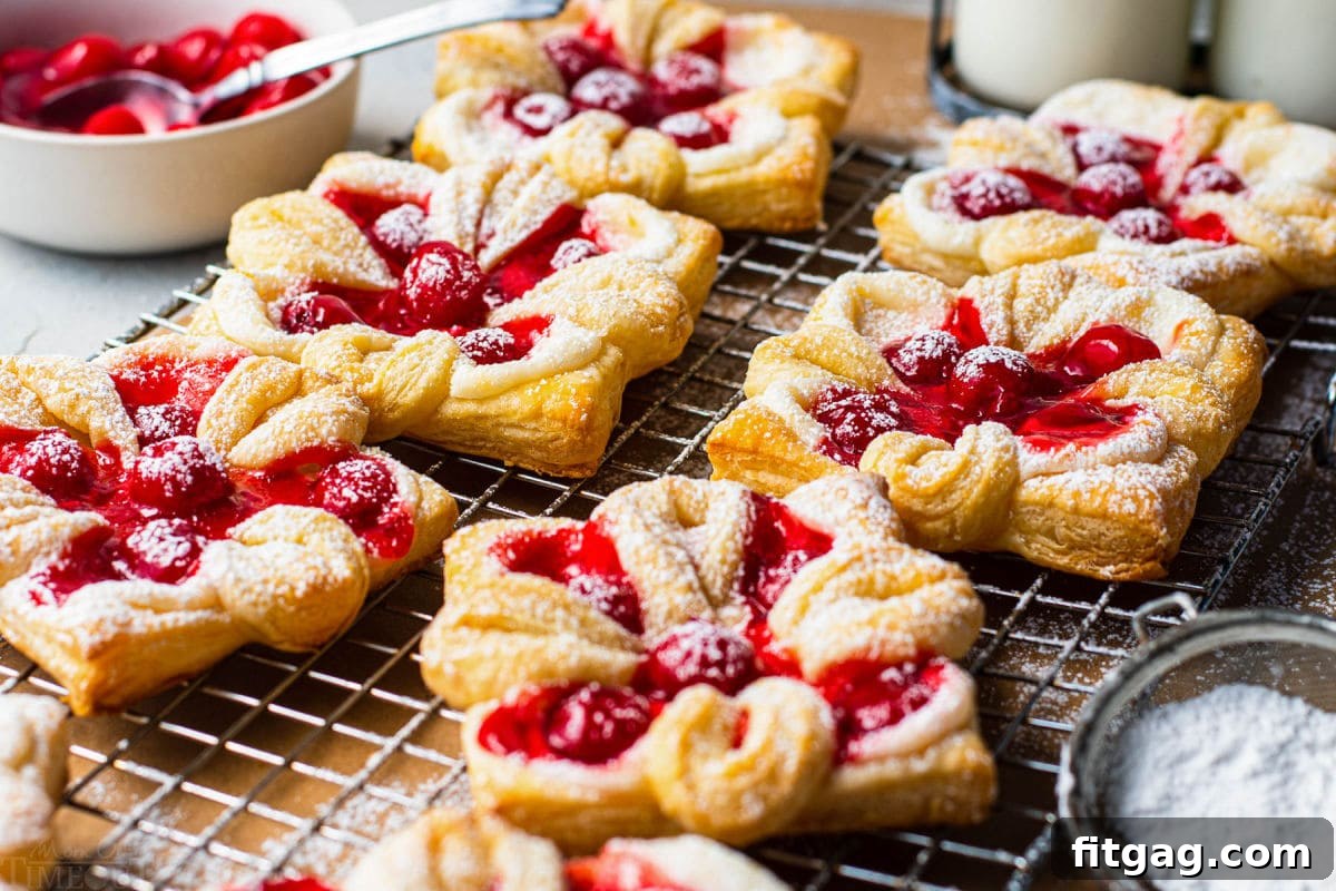 6 danishes with cherries baked and sprinkled with powdered sugar sitting on wire cooling rack
