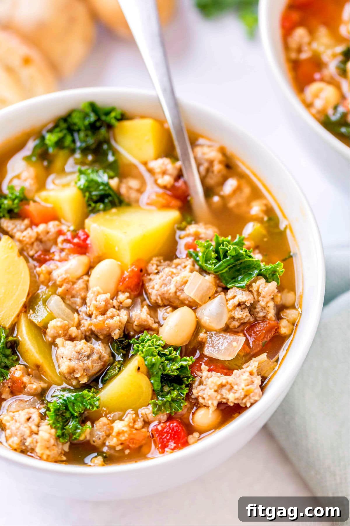Close-up view of the hearty sausage kale white bean soup in a white bowl with a spoon, showing off its rich texture.