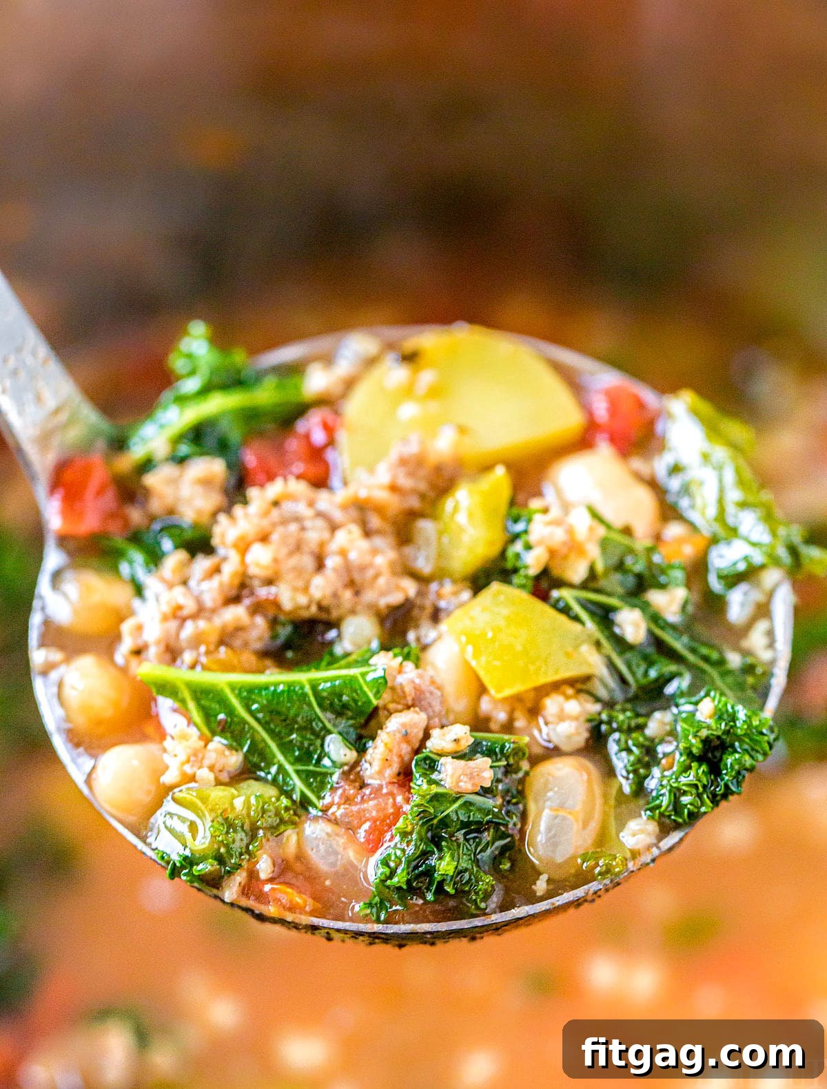 A ladle filled with rich, hearty sausage and kale soup, ready to be served.
