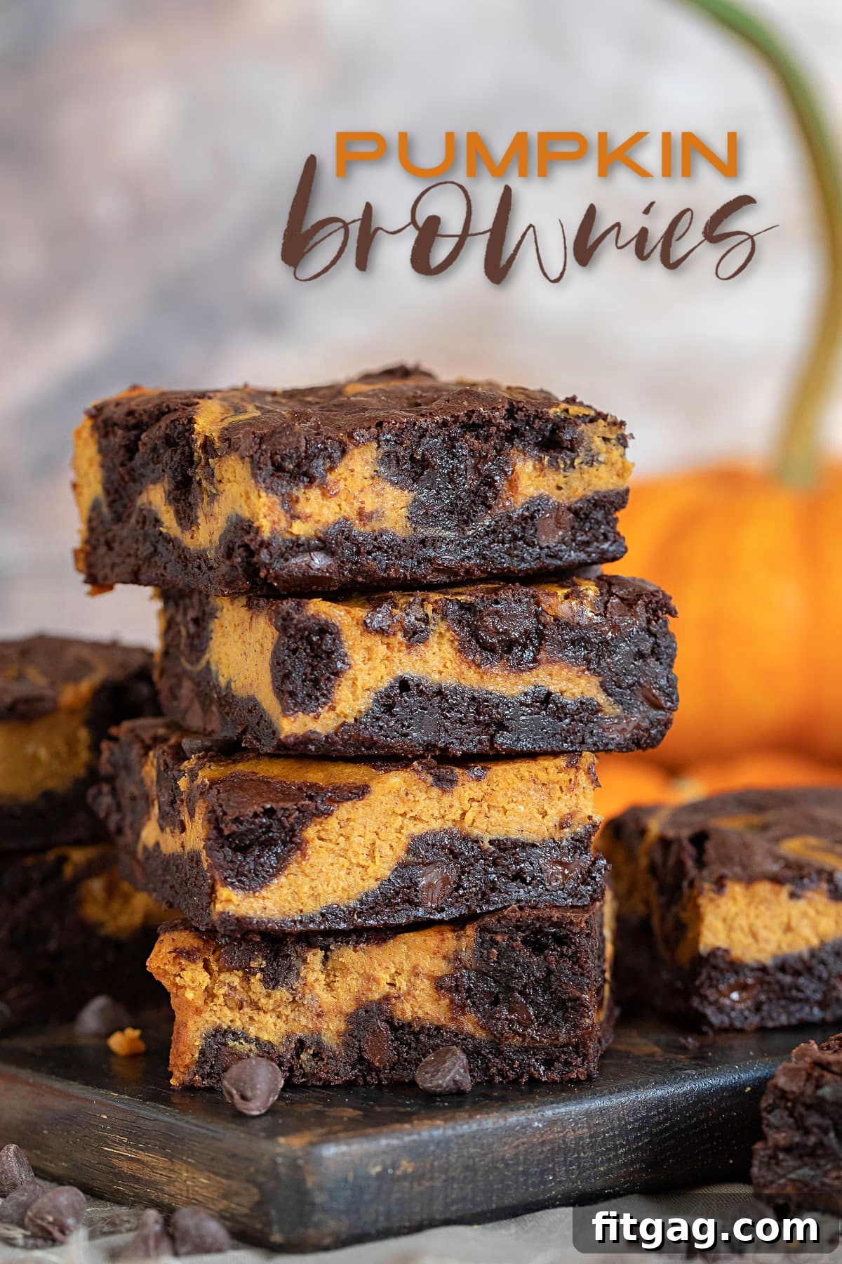 Pumpkin brownies stacked four high on a dark wood board with a pumpkin in the background, featuring a text overlay.