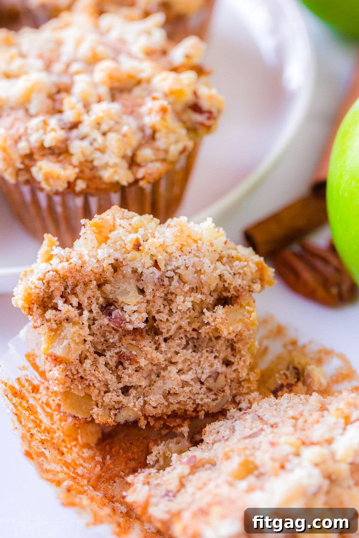 A perfectly baked apple muffin, split down the middle, showcasing its moist, spiced interior and tender apple chunks, still in its paper liner on a plate.