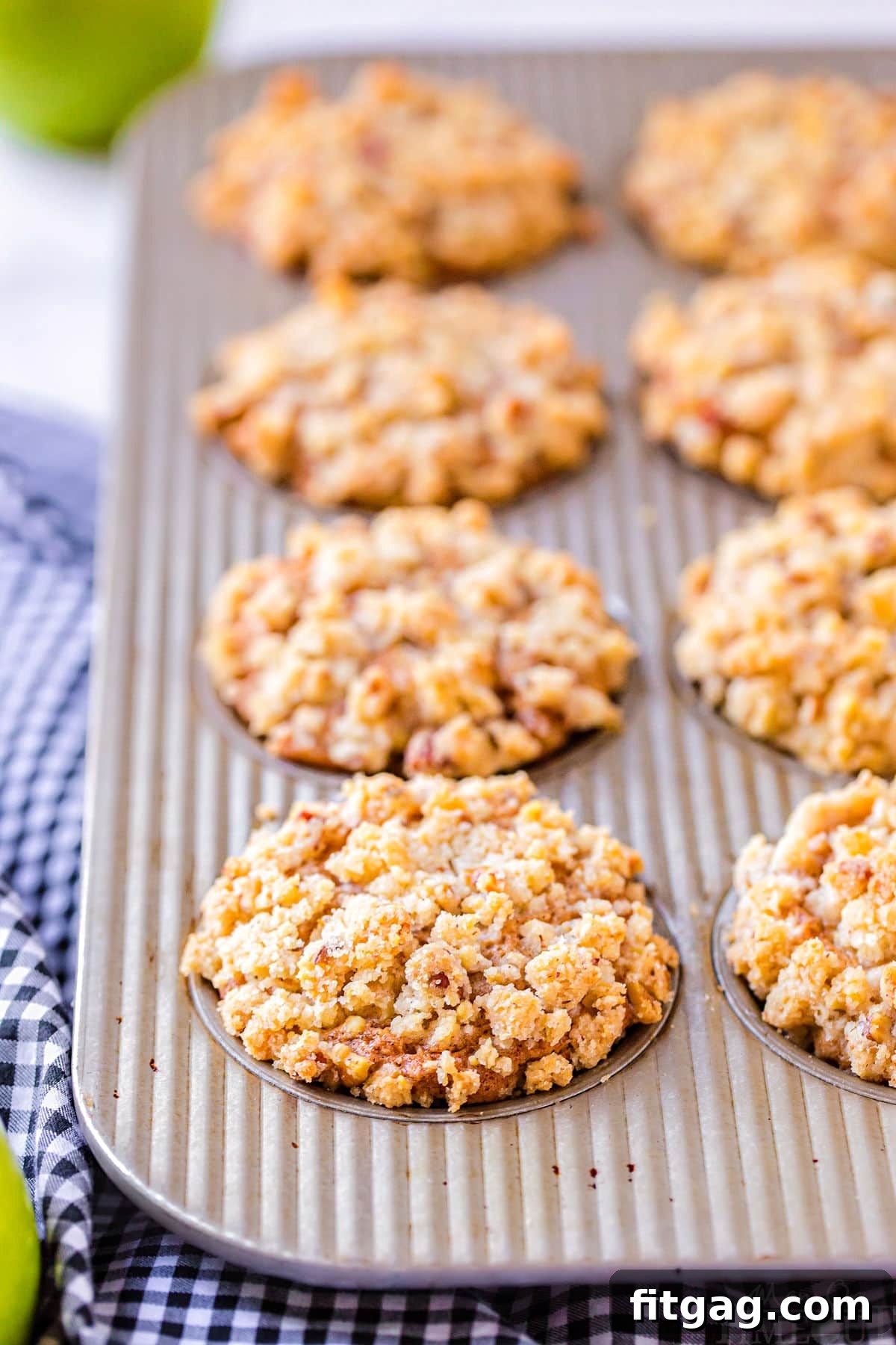 Freshly baked apple muffins, golden brown and topped with crumbly streusel, cooling in a muffin pan straight from the oven.
