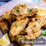 lemon pepper wings stacked in a pile garnished with parsley and lemon wedges sitting on parchment paper