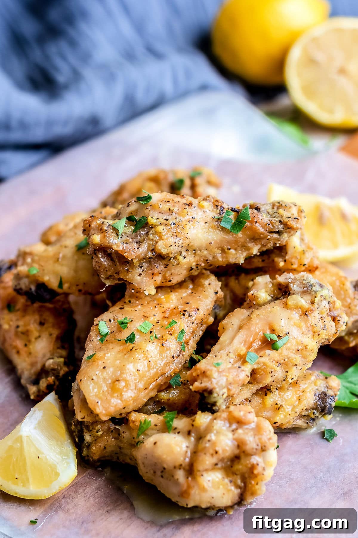 Irresistible Lemon Pepper Wings Baked or Air Fried 3 lemon pepper wings stacked in a pile with a blue napkin in the back with cut lemons
