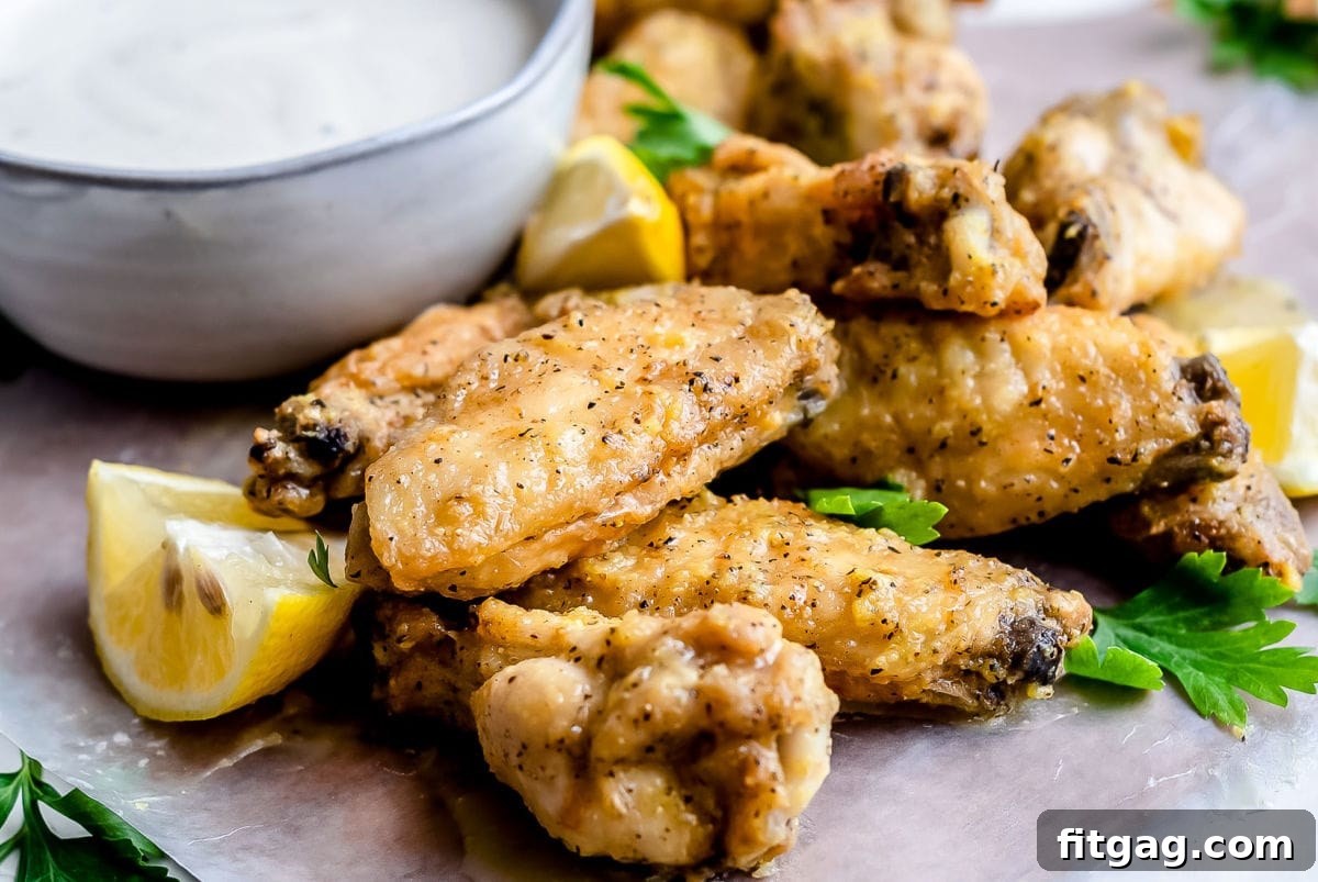 Irresistible Lemon Pepper Wings Baked or Air Fried 4 front view of baked chicken wings on gray plate garnished with chopped parsley and small bowl of ranch in background
