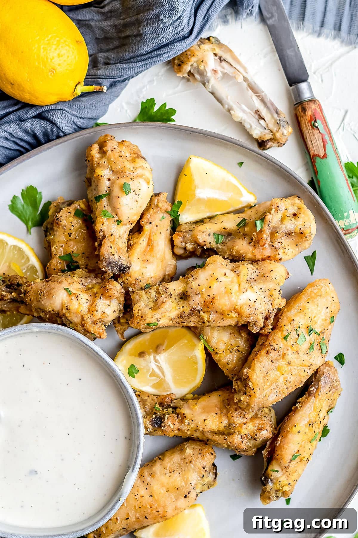 Irresistible Lemon Pepper Wings Baked or Air Fried 8 baked chicken wings on plate with ranch in small bowl and garnished with parsley and lemon top down view