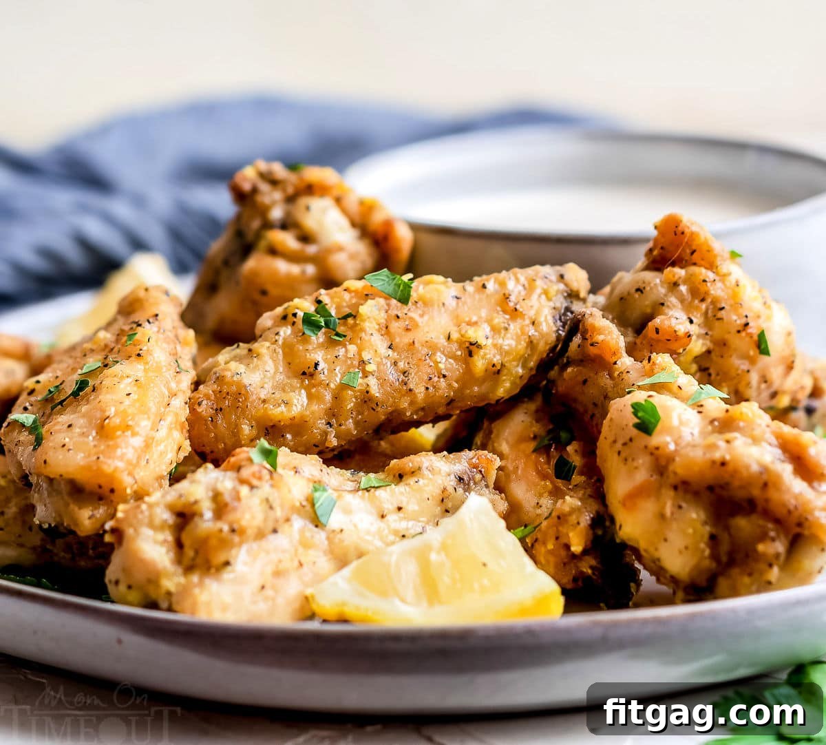 Irresistible Lemon Pepper Wings Baked or Air Fried 9 front view of baked chicken wings on plate with lemon wedges and blue napkin in the background