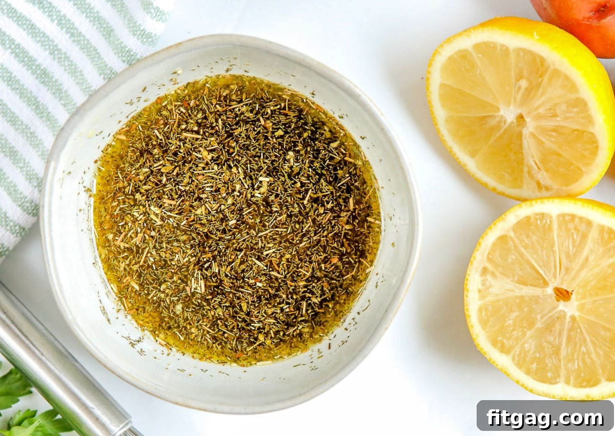 A small bowl containing the freshly prepared Greek chicken marinade, with bright lemon halves and fresh herbs artfully arranged beside it.