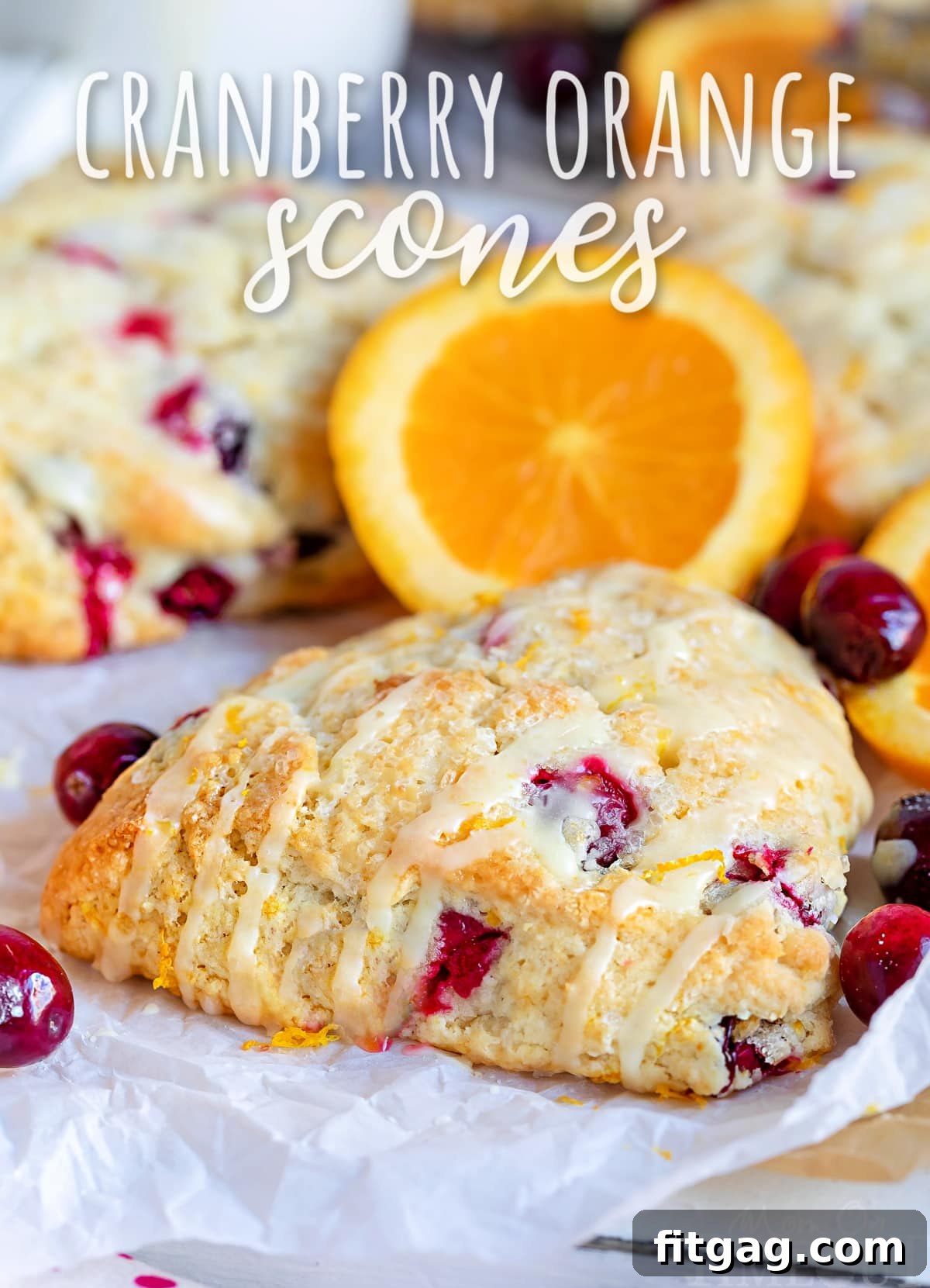 Zesty Cranberry Orange Scones 2 cranberry orange scone sitting on parchment paper with orange glaze drizzled on top with text overlay at top of image