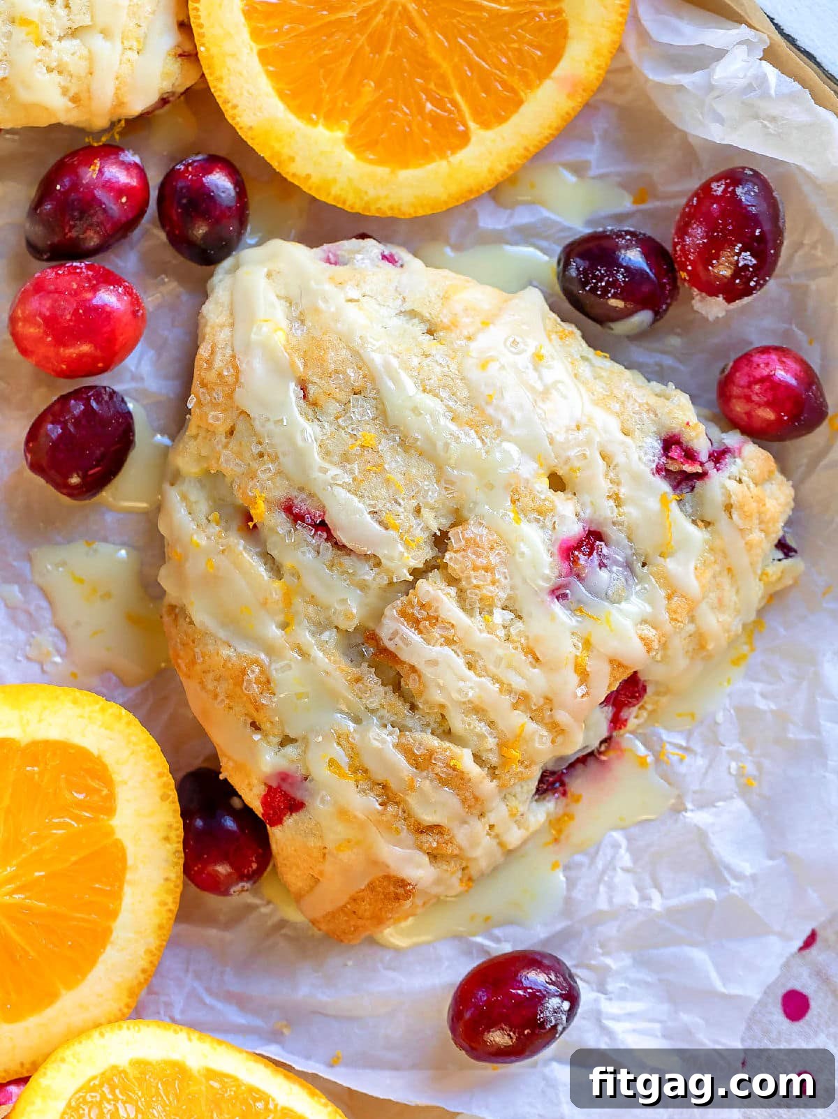 Zesty Cranberry Orange Scones 3 top down view of cranberry orange scone with cranberries scattered and orange slices on white parchment