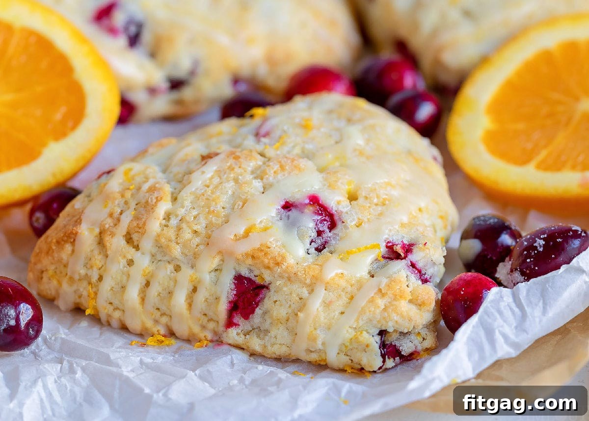 Zesty Cranberry Orange Scones 9 cranberry orange scones with orange glaze on top of white parchment with orange slices in background