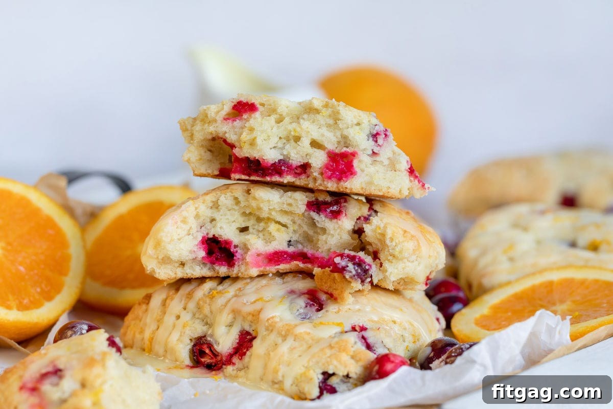 Zesty Cranberry Orange Scones 10 cranberry orange scones split up and sitting on parchment paper with orange slices and cranberries scattered about
