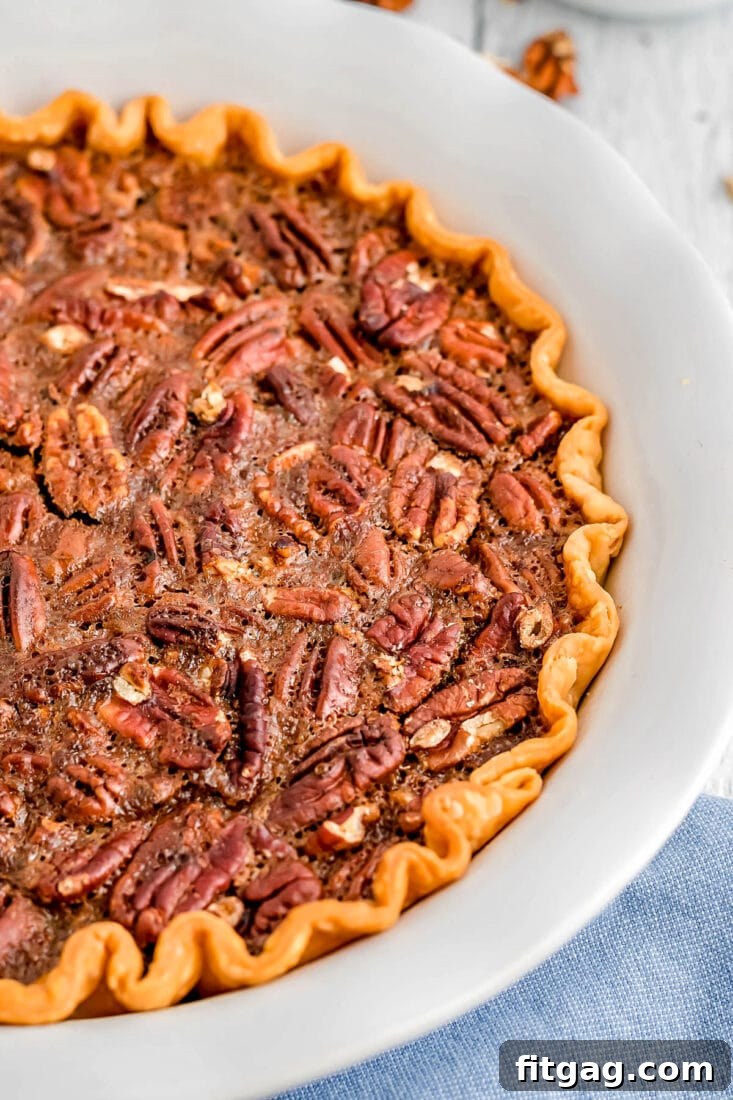 Decadent Maple Pecan Pie 9 A whole, beautifully baked Maple Pecan Pie, glistening with its rich, nutty top, resting invitingly in its pie plate, accompanied by a soft light blue napkin, ready to be sliced and served.
