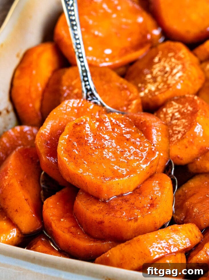 Close up shot of a spoonful of tender candied sweet potatoes, glistening with sauce, in a beige baking dish.