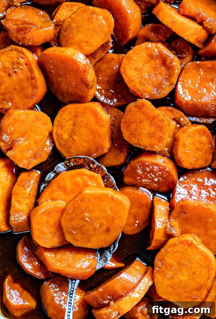 Top-down view of glistening candied sweet potatoes in a baking dish, with an antique spoon holding a portion at the bottom, showcasing the rich glaze.