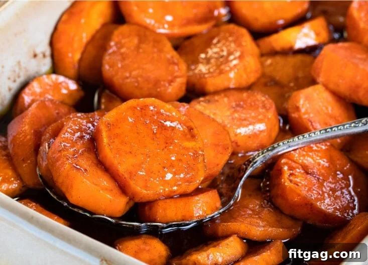 A generous spoonful of rich, glazed candied sweet potatoes being lifted from a beige baking dish, ready to be enjoyed.