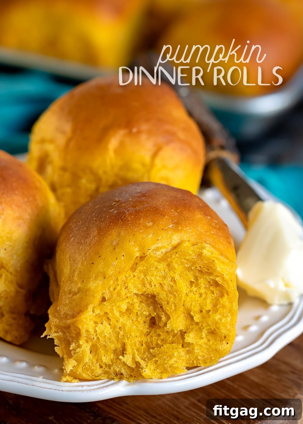 three pumpkin dinner rolls on a white plate with butter on the side