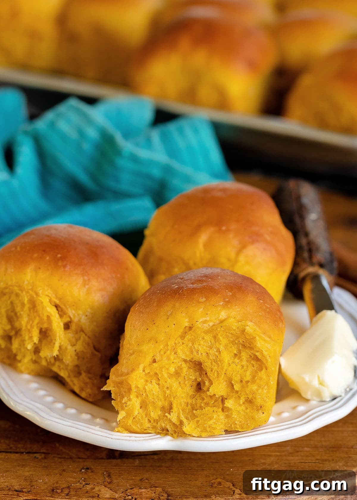 three pumpkin dinner rolls on a white plate with butter on the side and baking sheet in background