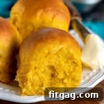 three pumpkin dinner rolls on a white plate with butter on the side