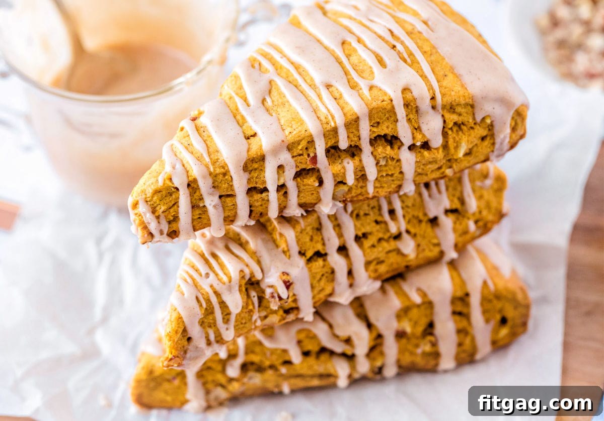 Stacked pumpkin scones, viewed from the top, featuring a generous drizzle of maple glaze over their golden surfaces.