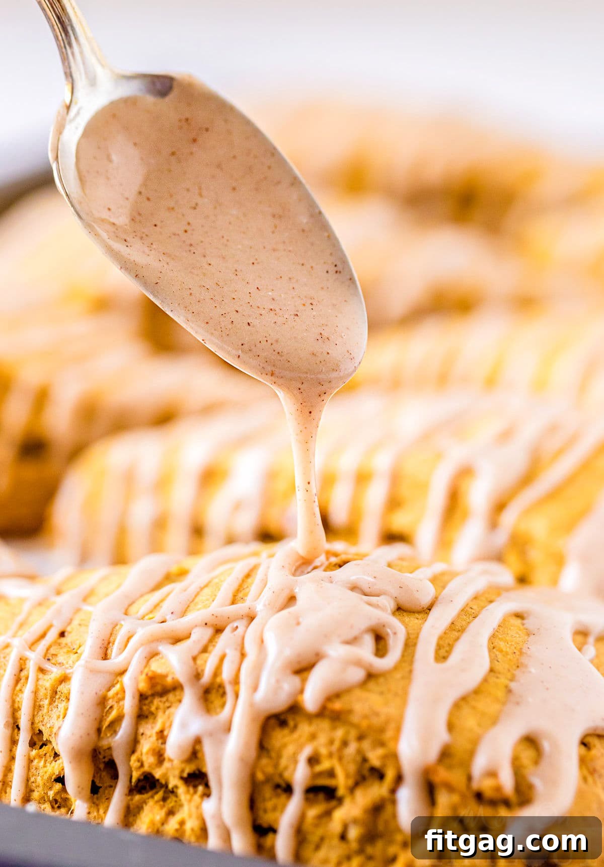 Close-up shot of maple cinnamon glaze being generously drizzled over warm pumpkin scones, creating an inviting finish.