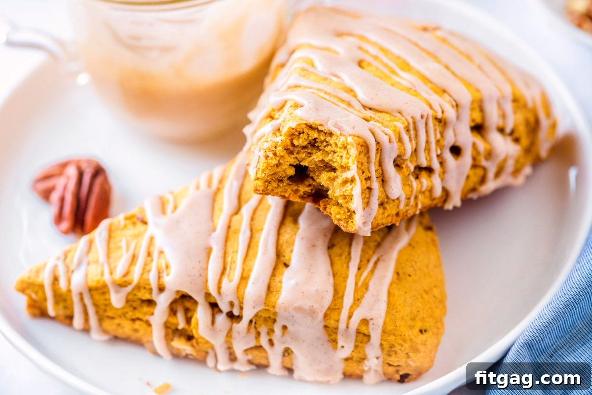 A single pumpkin scone with a bite taken, resting on a white plate next to a neatly folded blue napkin, highlighting its inviting texture.