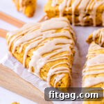 Pumpkin scones sitting on white parchment on a wood cutting board with a maple cinnamon glaze