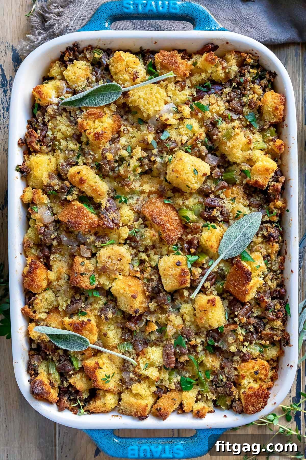 Ultimate Cornbread Dressing 3 A top-down view of a golden-brown cornbread stuffing in a baking dish, beautifully garnished with fresh sage leaves and thyme. This rich cornbread dressing is ideal for Thanksgiving, offering a blend of buttery, savory flavors with herbs, onions, celery, and optional sausage.