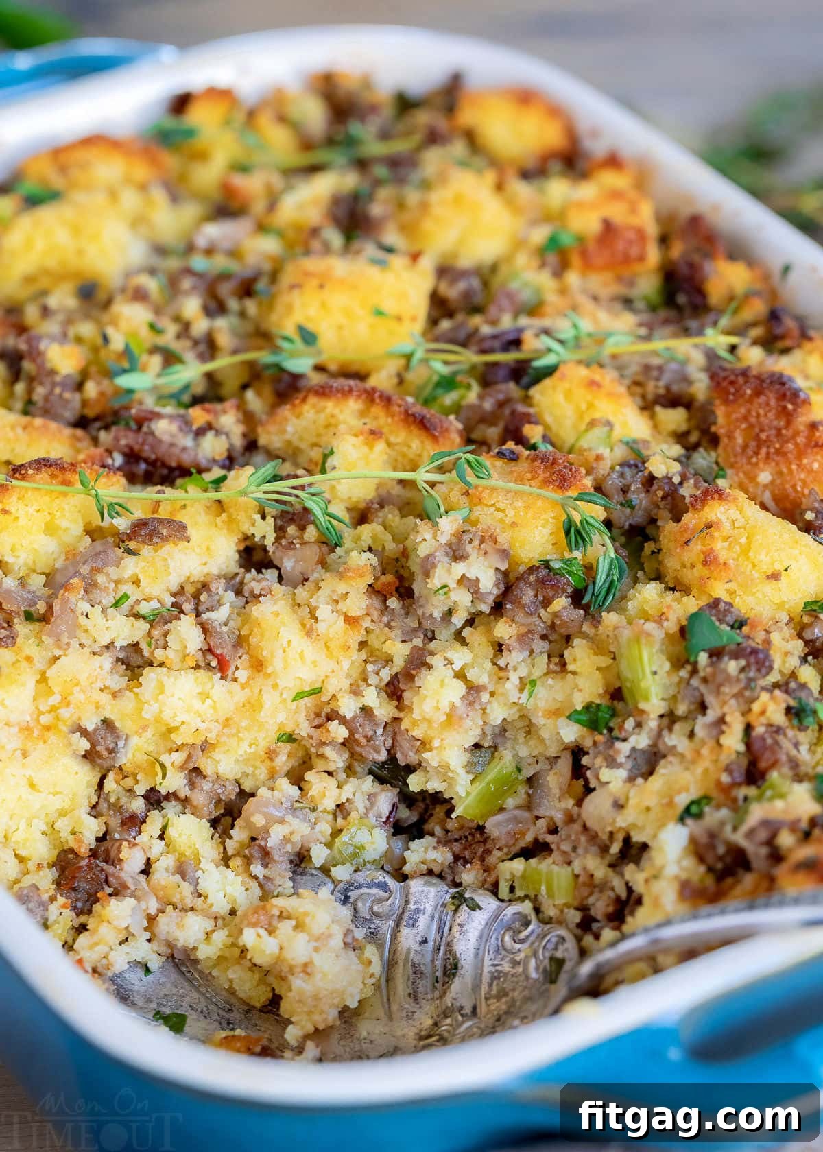 Ultimate Cornbread Dressing 4 A baking dish of warm, golden-brown cornbread stuffing with a scoop removed, revealing its moist and fluffy interior. This Thanksgiving side dish, bursting with buttery flavor, fresh herbs, onions, celery, and optional sausage, is a holiday classic.