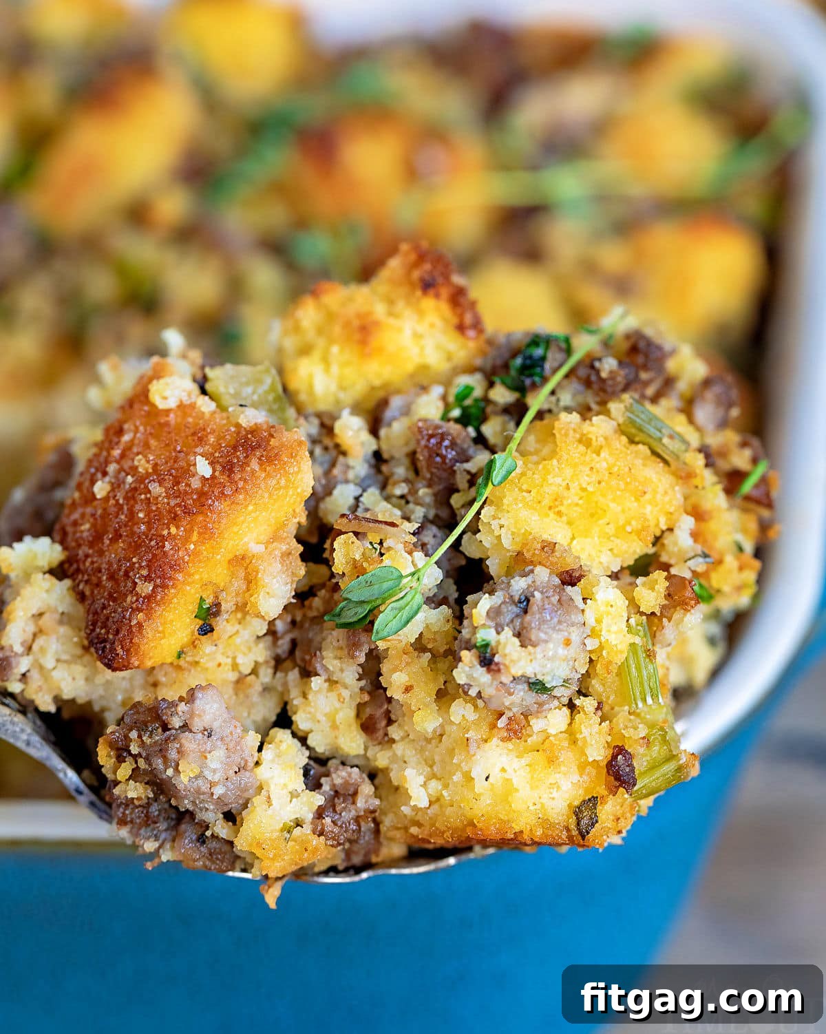 Ultimate Cornbread Dressing 5 A spoonful of moist cornbread stuffing being lifted from a casserole dish, with the full dish visible in the background. This savory cornbread dressing, a perfect Thanksgiving side dish, is made with fresh herbs, onions, celery, and optional sausage.