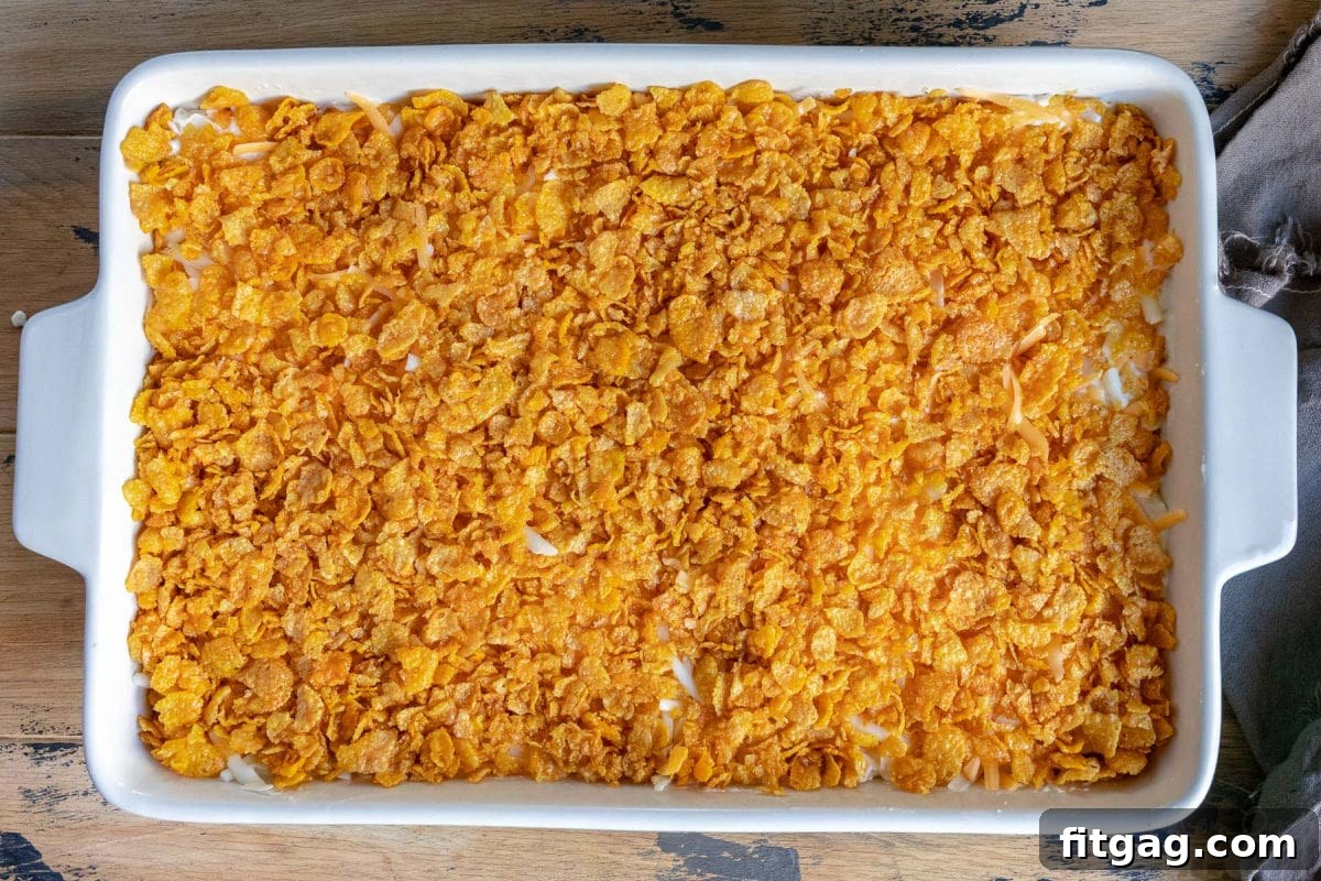A top-down view of an unbaked cheesy potato casserole in a baking dish, perfectly topped with a golden cornflake layer, ready to be placed in the oven.