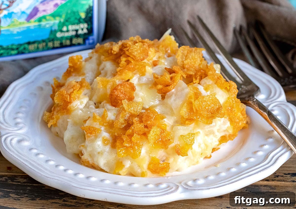A serving of cheesy potatoes on a white plate with a package of Challenge Butter in the background, emphasizing the quality ingredients used in the recipe.