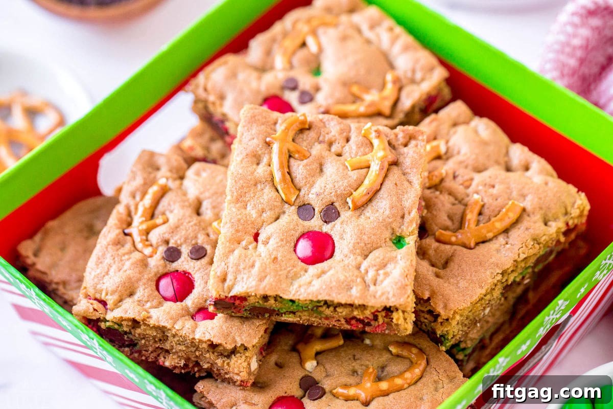 Magical Reindeer Cookie Bars 4 Close-up photograph of charming Reindeer Cookie Bars, each decorated with pretzel antlers, a colorful M&M nose, and mini chocolate chip eyes, carefully arranged in a festive Christmas gift box.