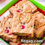 Reindeer cookie bars decorated with pretzels, M&Ms, and mini chocolate chips, artistically arranged in a festive Christmas box.