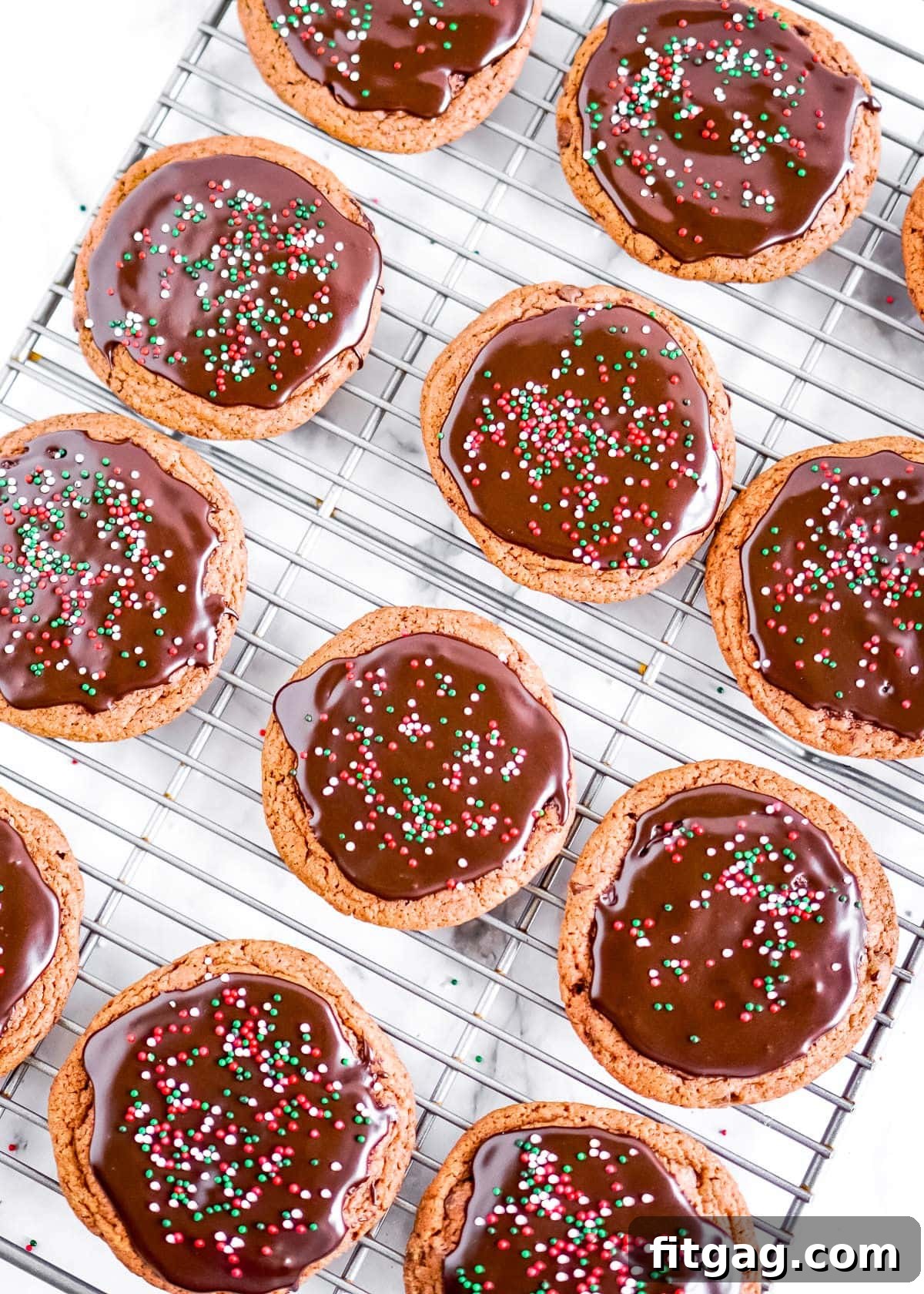 Top-down view of freshly baked chocolate cookies cooling on a wire rack, some already adorned with a glossy chocolate glaze.