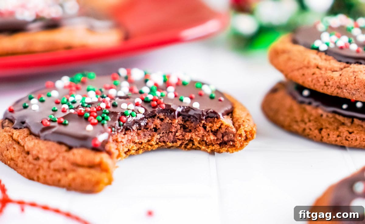 A chocolate cookie with a bite taken out, showcasing its soft interior, resting on a white surface with more glazed cookies blurred in the background.