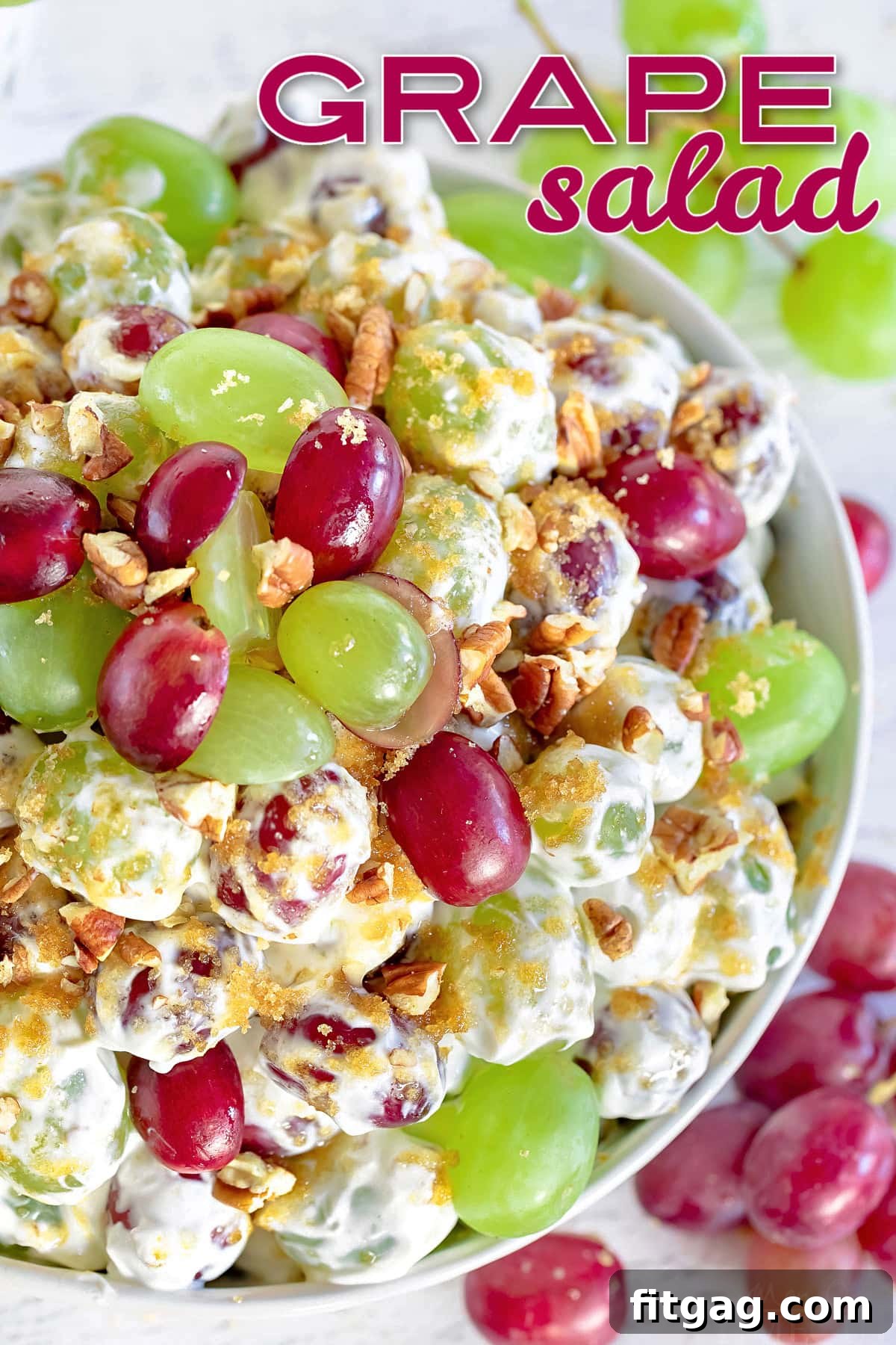 Creamy Grape Crunch 2 top down view of grape salad in clear bowl topped with cut grapes and pecans and brown sugar