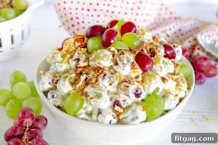 Creamy Grape Crunch 7 grape salad with creamy cream cheese dressing topping with brown sugar and pecans in white bowl with grapes around it